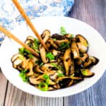 Sauteed shiitake mushrooms served on a white plate topped with green onions and butter ponzu sauce.