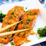 Miso sauce seared salmon served on a plate topped with green onions being picked up with chopsticks.