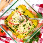 A piece of Tomato Garlic Baked Cod in a baking pan topped with melted Gruyere cheese and fresh parsley being picked up with a fork.