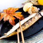 BBQ grilled pacific saury Japanese sanma shioyaki being picked up with a pair of chopsticks.