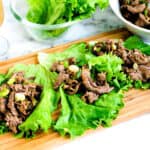 Asian inspired beef lettuce wraps topped with green onions served on a wooden plank, side view.