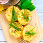 Cream cheese breakfast egg bites topped with sliced scallions served on a wooden board, top down shot.