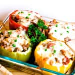 Ground beef stuffed bell peppers with tomato sauce baked in a baking dish topped with fresh parsley.