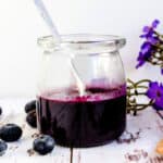 Blueberry Sauce served in a glass jar with a spoon inside.