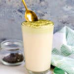 Matcha cream cheese foam being spooned into a cup of ice milk tea.