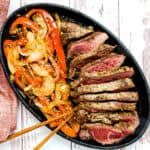 Top sirloin steak in black pepper sauce mixed with vegetables served on a cast iron plate being picked up with a pair of chopsticks, top down view.