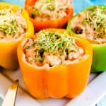 Feta ground beef stuffed bell peppers topped with sauce and alfalfa served on a white plate.