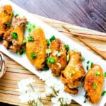 Garlic miso chicken wings topped with toasted sesame seeds and chopped green onions served on a white plate.