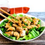 Japanese style pan fried chicken thigh served over a bed of lettuce being picked up with a pair of chopsticks.