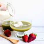 Matcha jelly served in a glass cup with heavy cream being poured on top.