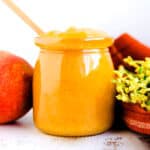 Homemade peach sauce in a glass jar with a wooden spoon.