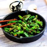 Asian style garlic green bean stir fry flavored with sesame oil served on a cast iron pan.