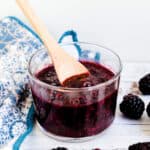 Homemade blackberry sauce served in a glass jar being scooped up with a wooden spoon.