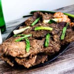 Korean BBQ marinated short ribs served on a cast iron plate topped with green onions and sesame seeds and a side of kimchi.