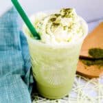 Matcha creme Frappuccino topped with whipping cream served in a plastic cup with a green straw.