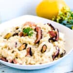 Seafood risotto made with rice served in a white bowl topped with fresh parsley.