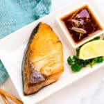 Japanese style pan seared hamachi yellowtail served on a plate with a Japanese style ponzu yuzu dipping sauce.