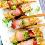 Bacon wrapped enoki yakitori being picked up with a pair of chopsticks.
