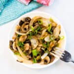 Sautéed mushrooms and onions topped with fresh chopped scallions served in a bowl, top angle.