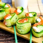 Cucumber wrapped cream cheese sushi roll made with sashimi grade salmon being picked up with a pair of chopsticks.
