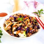 Egg roll in a bowl served in a white bowl with drizzle of Sriracha and garnish parsley.