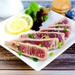 Japanese style seared yellowfin tuna tataki served on a white plate with a side salad.