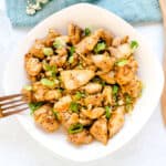 Spicy Garlic Pan Seared Chicken served in a white bowl topped with green onions and toasted sesame seeds