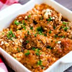 Top down shot of meatball with feta in a glass baking pan with chopped parsley on top.