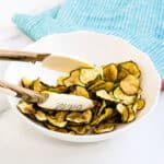 Crispy air fried vegetable zucchini chips seasoned with homemade salt and vinegar being picked up with tongs.