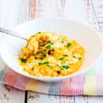 Cheesy cauliflower rice served in a bowl being scooped with a spoon.