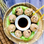 Cream cheese dumplings served on a wooden plate being cut in half with a pair of chopsticks, top down shot.