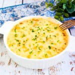 Chicken gratin served in a ramekin with melting cheese and fresh parsley sprinkled on top.