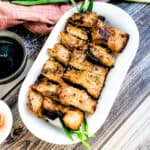 Korean BBQ garlic marinated pork belly grilled and served on a white plate with sliced green onions.