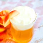 Peach cream cheese tea served in a glass cup with a slice of peach.