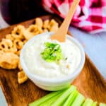 Homemade sour cream and onion dip served in a white bowl with pork rinds and celery.