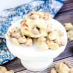 White chocolate almond clusters on a white pedestal, side angle.