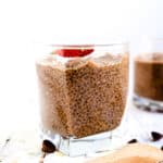 Chocolate chia seed pudding topped with fresh strawberries and shredded coconuts served in a glass cup with a wooden spoon, side view.