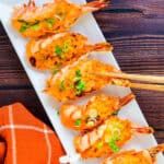 Dynamite shrimp served on a white plate topped with green onions, top down shot.