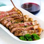 NY fillet pan seared steak finished in the oven topped with garlic butter and fresh parsley being cut into with a silver knife and fork.