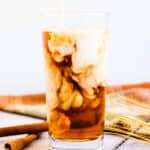 Iced vanilla chai tea latte served in a glass cup with cream being poured in.
