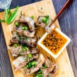 Korean style BBQ grilled pork belly, samgyeopsal-gui, being picked up with a pair of chopsticks being dipped into a sesame oil dipping sauce.