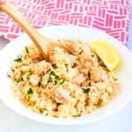 Langostino risotto served in a bowl topped with fresh parsley being scooped up with a spoon.