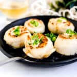 Pan sealed Japanese style scallops topped with chopped green onions and Japanese style mayo sauce served on a black plate.