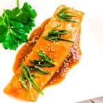 Soy ginger glazed salmon topped with green onions served on a plate.