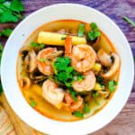 Tom yum soup served in a white bowl with a serving spoon.