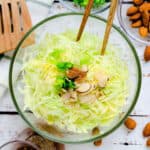 Asian Cabbage Salad topped with sliced almonds and green onions being picked up with a pair of chopsticks, top down.