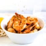 Pan fried shrimp seasoned with bay seasoning, garlic, lemon juice, and chili pepper served in a bowl with chopped parsley being sprinkled on.