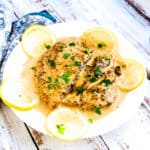 Creamy lemon chicken served on a white plate with slices of lemon, topped with cilantro.