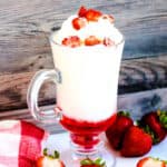 Strawberry Italian soda served in a glass topped with whipping cream and fresh chopped strawberries.