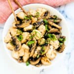Chicken mushroom stir fry served on a plate topped with green onions and toasted sesame seeds.